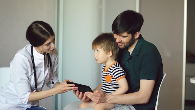 Medico della giovane donna che parla con il padre del ragazzino che utilizza il computer della compressa nello studio medico