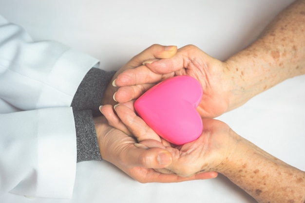 Medico delle giovani donne e mani di eldely che tengono cuore rosa.