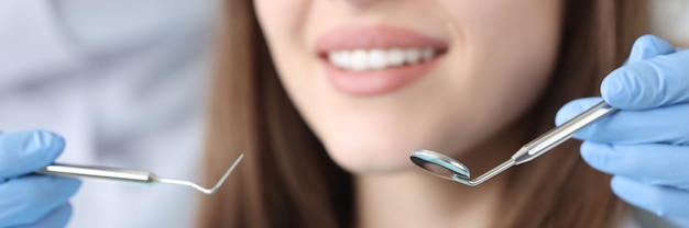 Medico dentista che tiene gli strumenti dentali davanti al paziente femminile in primo piano della clinica