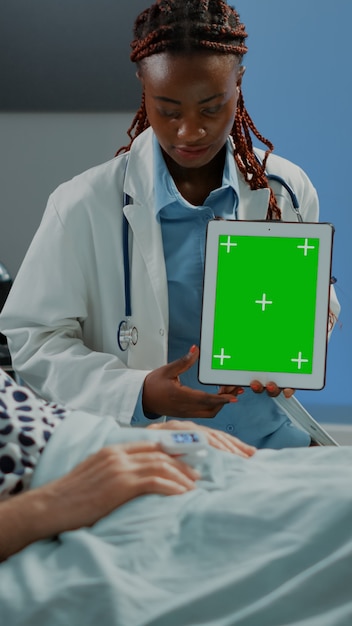 Medico di analisi che mostra tablet con schermo verde al paziente