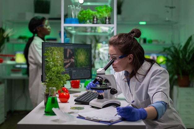 Medico di biochimica che esamina test chimico utilizzando il microscopio per ricercatore genetico. Specialista biologo scopre piante ogm organiche mentre lavora nel laboratorio alimentare di microbiologia.