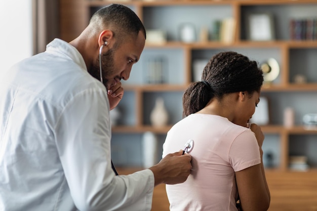 Medico di medicina generale dell'uomo arabo che controlla i polmoni della donna malata con lo stetoscopio