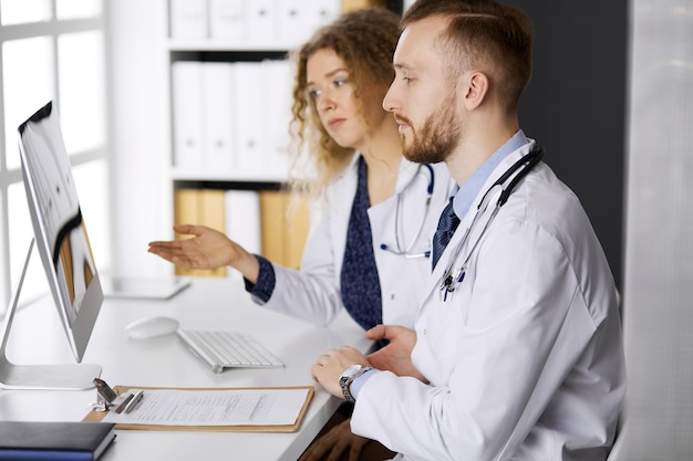 Medico di sesso maschile con un collega che discute la terapia attuale della malattia mentre è seduto al posto di lavoro in clinica. Lavoro di squadra in medicina.