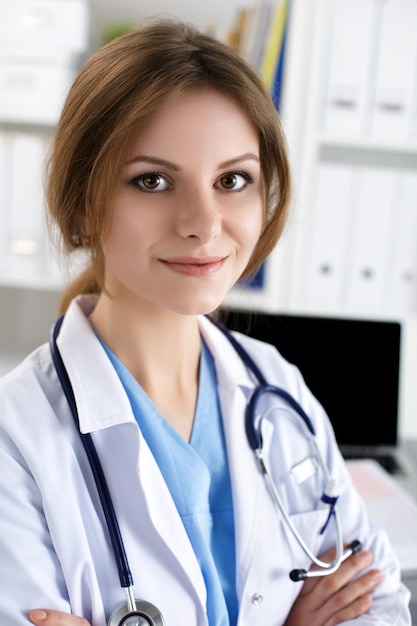 Medico di terapista di medicina femminile in piedi con le mani incrociate sul petto che tiene lo stetoscopio in ufficio