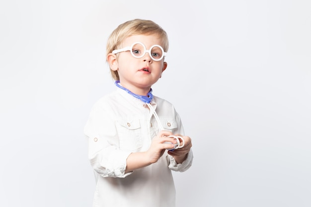 Medico divertente del bambino con gli occhiali e lo stetoscopio su fondo bianco con lo spazio della copia