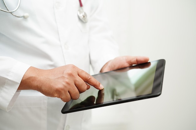 Medico donna asiatica che tiene telefono cellulare o tablet per il metodo di ricerca del paziente di trattamento in ospedale