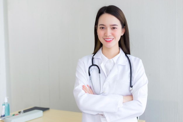 Medico donna asiatica professionale che indossa una veste bianca e uno stetoscopio In piedi con le braccia incrociate felice
