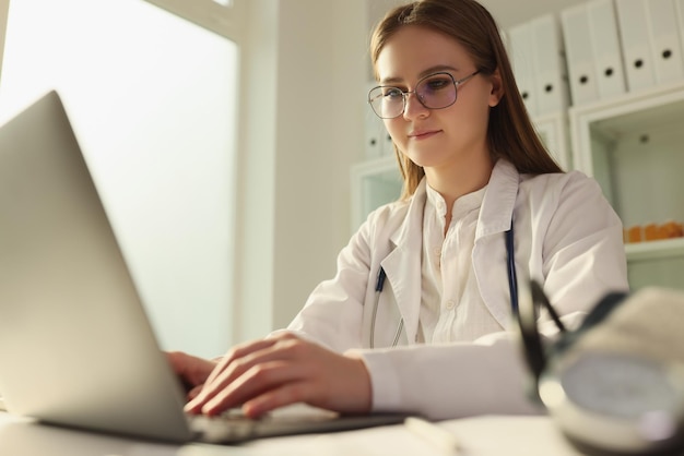 Medico donna con gli occhiali che lavora al computer portatile in clinica consultazione medica remota dei pazienti