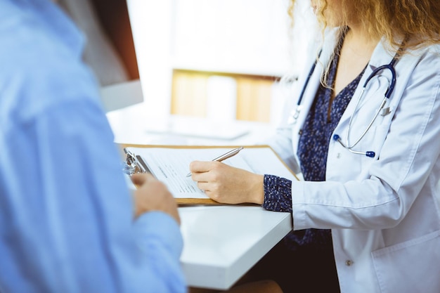 Medico donna e paziente che discutono dell'attuale esame sanitario mentre si siedono in una clinica soleggiata, primo piano.