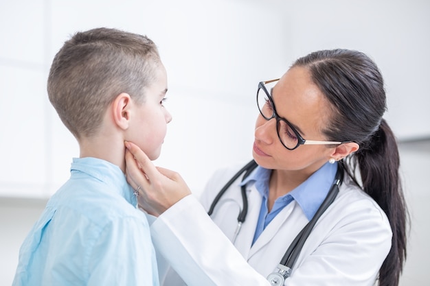 Medico donna esaminando le tonsille del giovane ragazzo in studio medico.