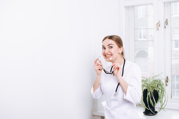 Medico donna felice in camice bianco con uno stetoscopio sullo sfondo della finestra