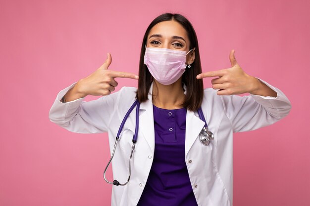 Medico donna indossa maschera medica e stetoscopio isolato sulla parete.