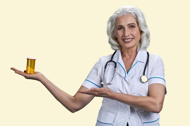 Medico donna matura felice che mostra una bottiglia di pillole medico femminile che offre pillole mediche contro bianco