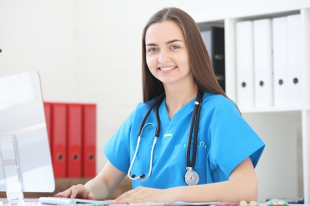 Medico donna seduta in ufficio al tavolo, guardando la fotocamera e sorridente