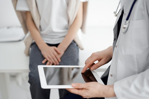 Medico e bambino paziente. Il dottore sta usando il computer tablet ed è pronto a esaminare il ragazzo. Il concetto di salute ideale in medicina.