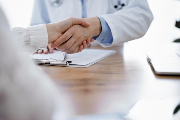 Medico e paziente che stringono le mani sopra il tavolo di legno in clinica. Concetto di medicina