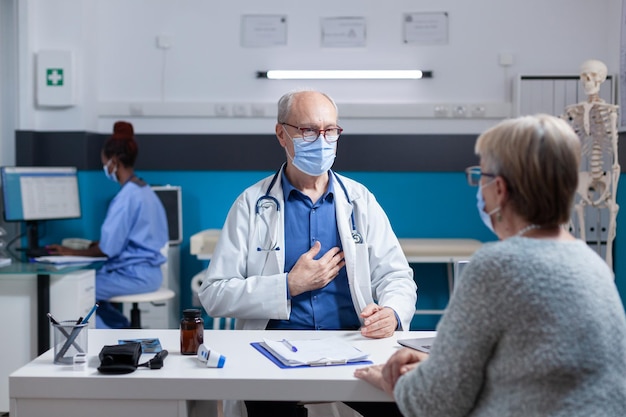 Medico e paziente con maschera facciale che discutono sulla diagnosi medica. Medico di medicina generale che parla con una donna anziana alla visita di controllo annuale durante la pandemia di coronavirus.