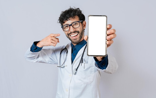 Medico felice che mostra lo schermo del telefono cellulare alla fotocamera Medico sorridente che mostra lo schermo del telefono cellulare che punta il dito isolato