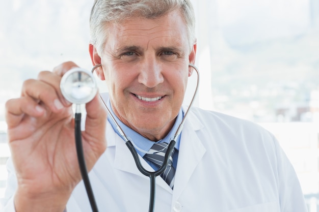 Medico felice che sorride alla macchina fotografica e che mostra il suo stetoscopio