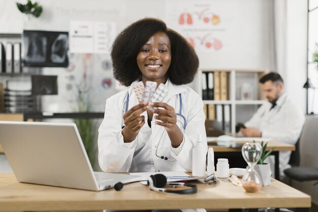 Medico femminile africano che tiene le pillole e sorride sulla macchina fotografica