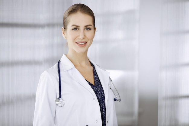 Medico femminile allegro che sta in clinica. Ritratto di medico donna sorridente amichevole. Servizio medico perfetto in ospedale. Concetto di medicina.