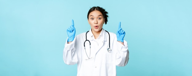 Medico femminile asiatico emozionante del lavoratore medico che indica le dita verso l'alto indossando guanti sterili e uniforme st