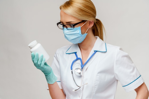 Medico femminile che indossa i guanti protettivi del lattice e della maschera e che tiene latta delle pillole
