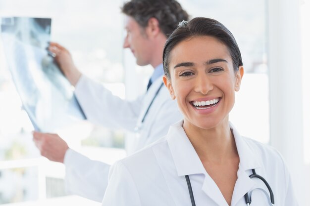 Medico femminile che sorride alla macchina fotografica mentre il suo collega che esamina raggi X