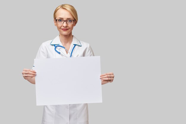 Medico femminile che tiene un foglio di carta bianco o un poster