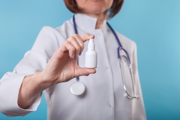 Medico femminile che tiene uno spray nasale su fondo blu