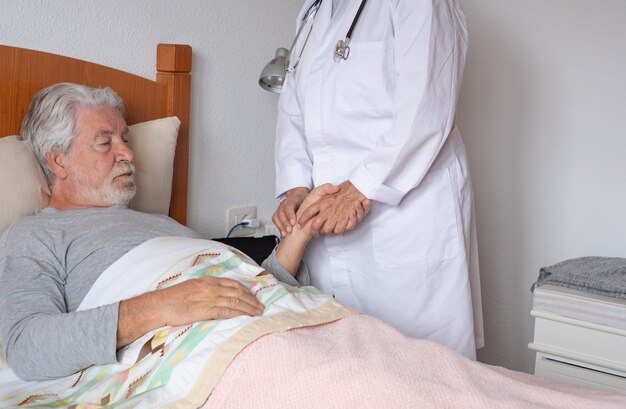 Medico femminile che visita un paziente anziano a casa controllando la temperatura. Uomo anziano preoccupato sdraiato a letto