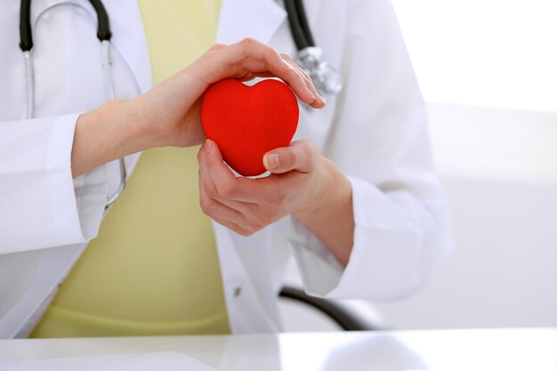 Medico femminile con lo stetoscopio che tiene il cuore. Coppia di pazienti seduti in background