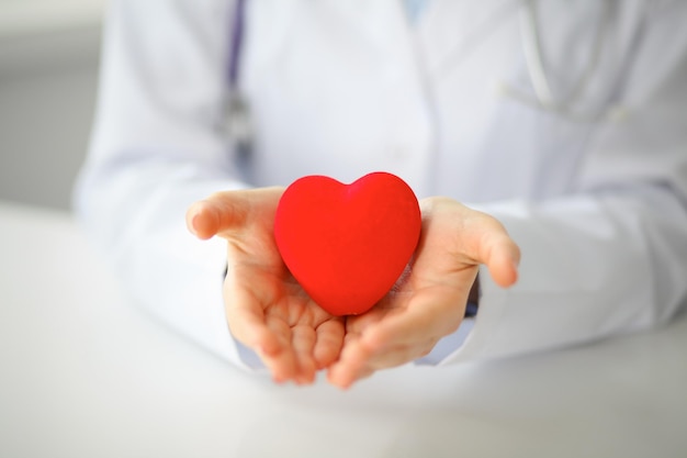 Medico femminile con lo stetoscopio che tiene il cuore. Coppia di pazienti seduti in background