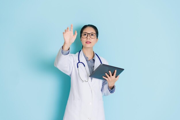 medico femminile in piedi e toccando lo schermo con uno sfondo blu isolato che tiene il suo tablet.