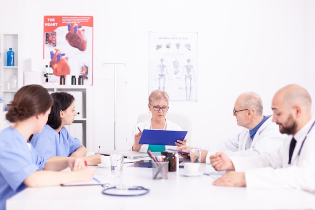 Medico femminile maturo che informa il suo personale medico sulla diagnosi del paziente nella sala conferenze. Terapeuta esperto della clinica che parla con i colleghi della malattia, professionista della medicina