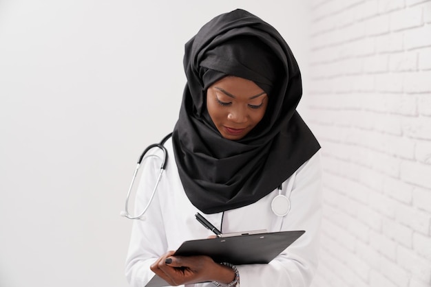 Medico femminile musulmano africano che scrive nella cartella