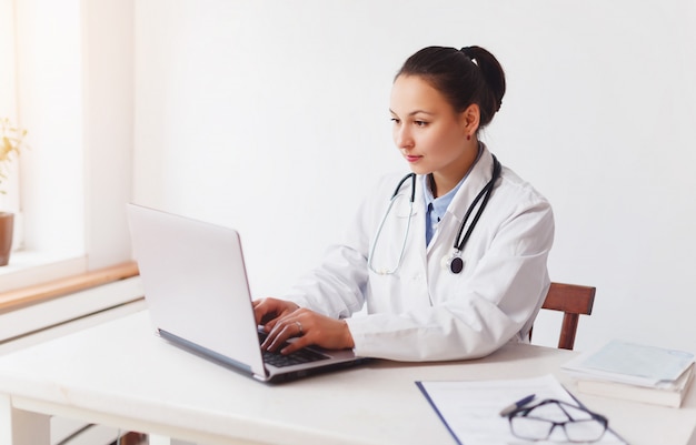 Medico femminile nel suo luogo di lavoro che lavora con il computer portatile