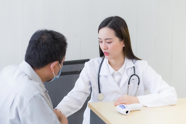 Medico femminile professionista asiatico che parla con un paziente uomo del suo dolore e dei suoi sintomi