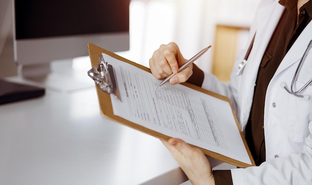 Medico femminile sconosciuto che utilizza appunti nella clinica soleggiata. Servizio medico perfetto in ospedale.