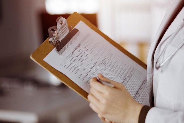 Medico femminile sconosciuto che utilizza appunti nella clinica soleggiata. Servizio medico perfetto in ospedale.