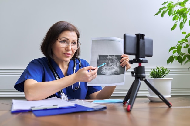 Medico femminile sicuro maturo che fa consultazione video tramite smartphone