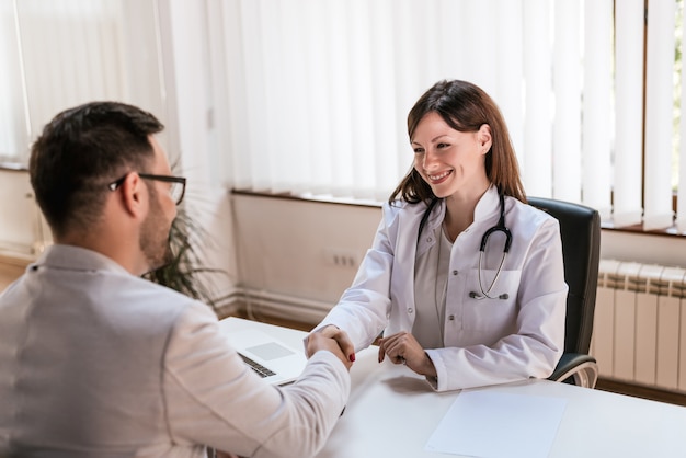 Medico femminile sorridente alla clinica che dà una stretta di mano al suo paziente