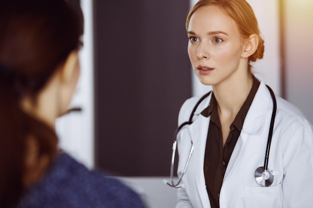 Medico femminile sorridente allegro e donna paziente che discutono l'esame di salute corrente mentre si siedono in clinica. Servizio medico in ospedale. Concetto di medicina.