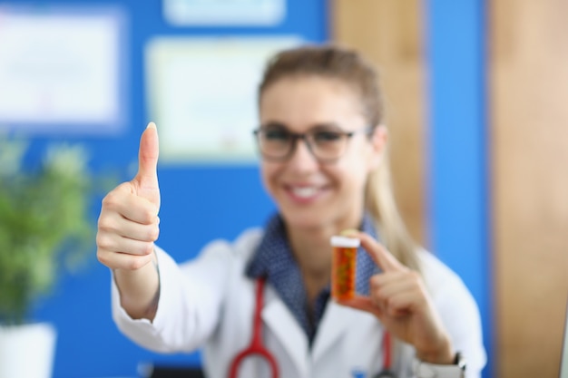 Medico femminile sorridente che mostra i pollici in su e che tiene il farmaco