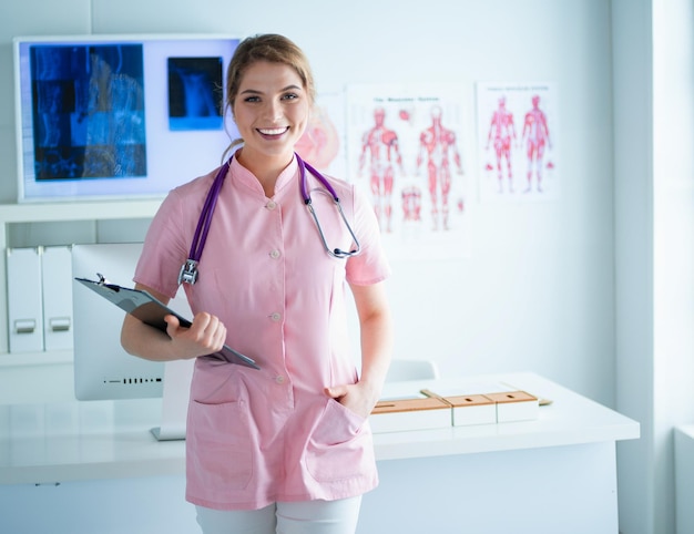 Medico femminile sorridente con una cartella in uniforme che sta all'ospedale