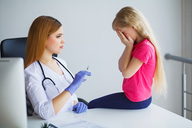 Medico femminile sorridente dei giovani e il suo piccolo paziente con l'orsacchiotto.