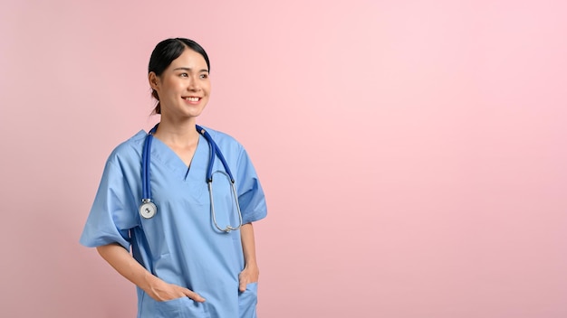 Medico femminile sorridente e in piedi sullo sfondo rosa isolato