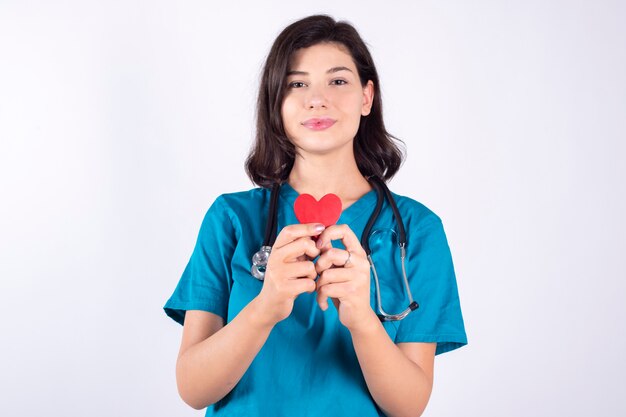 Medico femminile splendido che usando un cuore rosso su spazio bianco