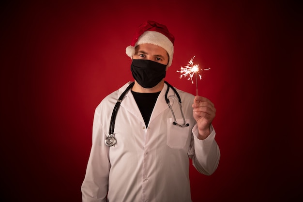 medico in cappello di Babbo Natale con maschera facciale che tiene le stelle filanti in fiamme