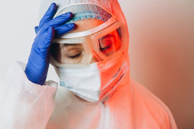 Medico in divisa protettiva, occhiali, guanti su uno sfondo blu in luce al neon. Ritratto di Close-up di un medico in neon rosso. l'uomo stanco sta combattendo un coronavirus. COVID 19